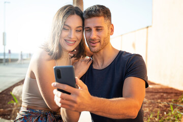 Young happy couple taking selfie with mobile phone or talking online with friends, smiling to the smartphone. Summer time.