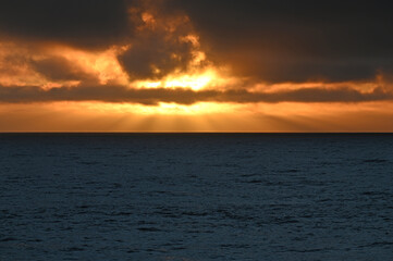 Sunset sun rays on flat Pacific Ocean.