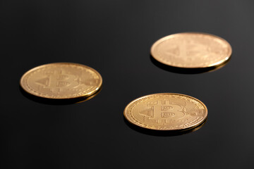 Detail studio shot of three golden bitcoins laying on black reflective surface. Concept for electronic money, crypto currency, blockchain investment, wealth, mining, financial markets.