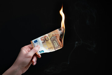 Studio shot of left hand holding a burning fifty Euro bank note. Concept for inflation, eurozone...