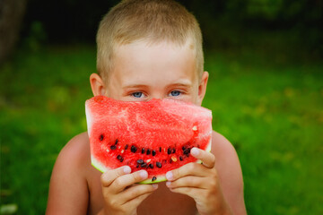 Portrait of a boy holding a slice of watermelon in front of his face on a green background of...