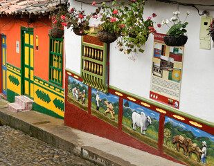 Fototapeta na wymiar Guatape, Colombia: Calle del Recuerdos is a cobblestone pedestrian street that passes between colorful tile-roofed buildings decorated with zocalos (friezes) and hanging pots of flowers