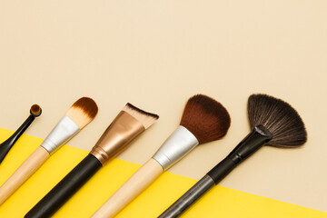 Flat lay composition of makeup brushes on yellow and beige background. Eye shadow brush, multi-function brush, concelear brush and highlighting brush.