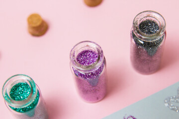 Composition of multicolor sparkling decorative eye shadows with hearts drawn on gray and pink background. Close up of glitter in jars.