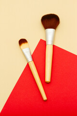 Flat lay composition of makeup brushes on yellow and beige background. Concelear brush and highlighting brush.