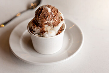 delicious chocolate and vanilla italian ices in paper cup on white saucer with white table and spoon