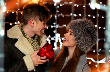 Closeup of cute , young couple boyfriend giving his girlfriend a present, looking each other in the eyes Winter season, valentines day concept .