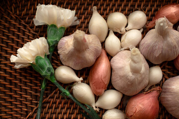 closeup of garlic and shallots in brown wicker basket with carnations