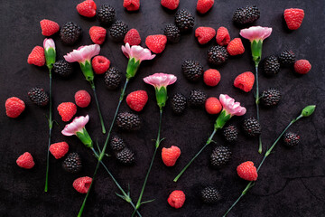 red raspberries, blackberries, and pink carnations on black background