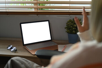 Rear view of young woman having video call on computer laptop in living room.
