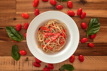fresh cooked pasta in white bowl on wood table with cherry tomatoes and basil surrounding