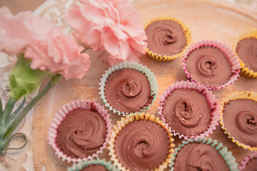 closeup homemade peanut butter cups in pastel wrappers and pink carnations