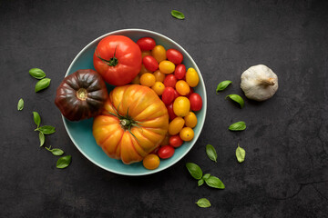variety of tomatoes in blue bowl on black background with basil and garlic 