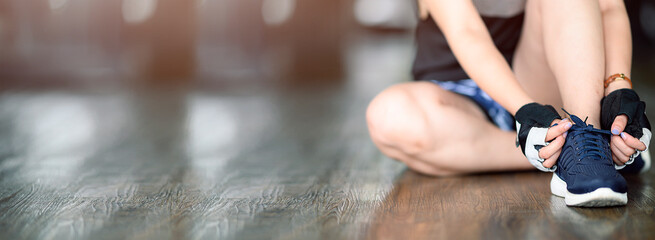 Young caucasian woman is tying her shoelaces before exercise at gym.