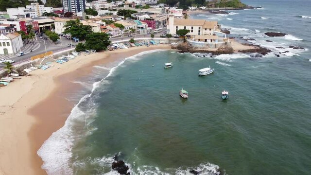 Aerial view of Coastline revealing Red River Beach in Salvador of Carnival, state of Bahia Brazil. Sea with waves and rocks. Tropical Urban environment with streets and cars passing by.