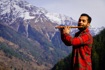 man playing Indian flute in mountains