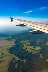 Obraz premium View of airplane wing, blue skies and green land during landing. Airplane window view.