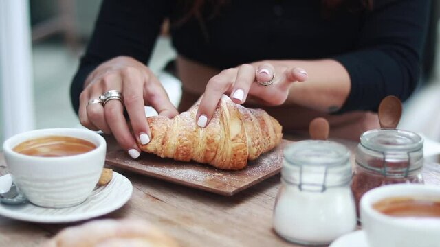 Young woman having delicious breakfast with coffee and croissant at table in cafe, closeup