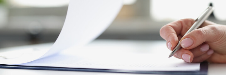 Woman hand signing documents on clipboard with ballpoint pen closeup