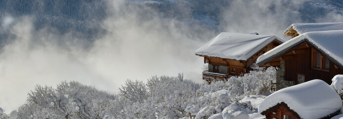 wooden chalets  in alpine village covered with snow overlooking cloudy valley landscape