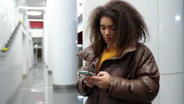 African female waits for a train in the subway and uses a smartphone, surfs the internet, a young student goes to study at the university, public transport.