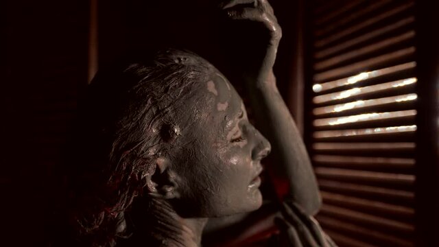mud wrap in spa salon for women, young lady is smearing clay on her skin, closeup portrait