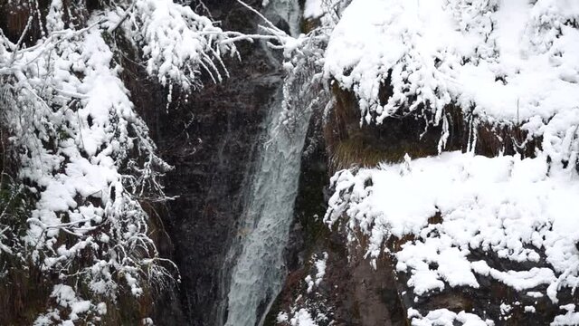 Slow motion shot of the water of the Jana waterfall flowing during the snowfall in winter at Kullu in Himachal Pradesh, India. View of the waterfall during the snowfall. Winter background.	