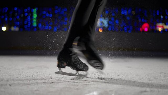 Slow motion, figure skating on ice, professional man gymnast performs a trick on ice, man spinning on skates, a view of the legs.
