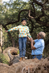 Happy grandfather holding hand of playful grandson walking on tree trunk at park
