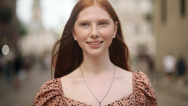 Beautiful Young Woman with long red hair walking on the street look at camera. Female model with natural beauty and lovely freckles on her Face