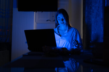 dinner late at night at home while working remotely online. Portrait of a young beautiful girl eating food from the delivery and working on her laptop.