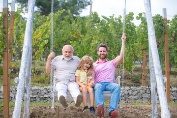 Men generation: grandfather father and grandson are swinging, looking at camera and smiling....