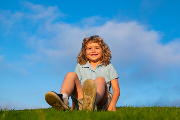 Fototapeta premium Little boy child with a cute expression face sitting on grass. Cheerful kid having fun on green summer meadow.