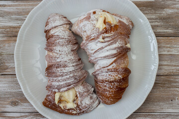 Sweet lobster tails with cream in a white serving plate. Italian pastry. Isolated on wooden background with white brush strokes