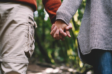 Close up of couple holding hands with green forest nature background. Concept of love and relationship with adults man and woman heterosexual people in contact.