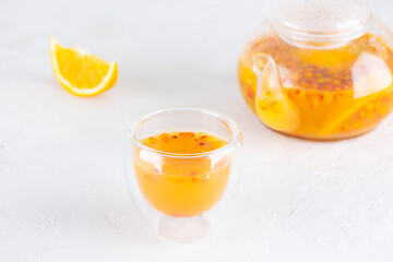Sea buckthorn tea with orange juice in a glass and teapot on the table.