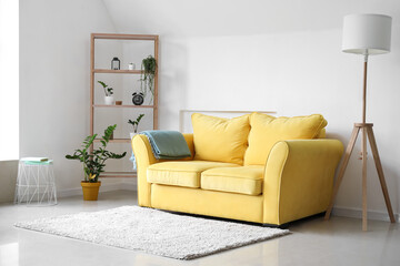 Interior of light living room with yellow sofa, shelving unit and plants