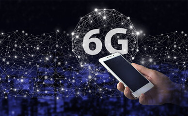 Wireless systems and internet of things IOT . Hand hold white smartphone with digital hologram 6G sign on city dark blurred background. Abstract world network connection, internet global connection