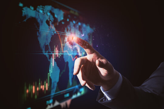 Close up of businessman hand pointing at glowing blue business forex chart and map interface on dark background. Trade, finance, analysis, growth, technology and innovation concept.