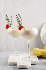 Cocktail glasses with sweet banana milk shake beverage, raspberries and coconut on white marble board