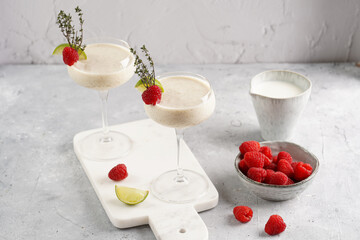 Cocktail glasses with sweet banana milk shake beverage, raspberries and coconut on white marble board