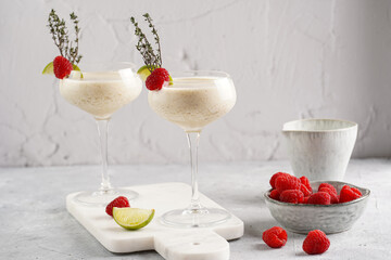 Cocktail glasses with sweet banana milk shake beverage, raspberries and coconut on white marble board