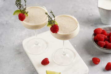 Cocktail glasses with sweet banana milk shake beverage, raspberries and coconut on white marble board