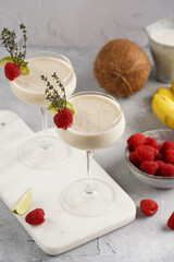 Cocktail glasses with sweet banana milk shake beverage, raspberries and coconut on white marble board
