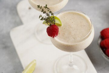 Cocktail glasses with sweet banana milk shake beverage, raspberries and coconut on white marble board