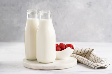 Two bottles with non-dairy milk and raspberries on round marble board