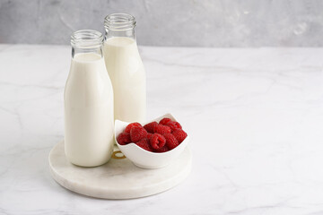 Two bottles with non-dairy milk and raspberries on round marble board