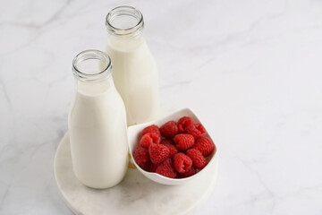 Two bottles with non-dairy milk and raspberries on round marble board