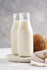 Two bottles with non-dairy milk and coconut on round marble board