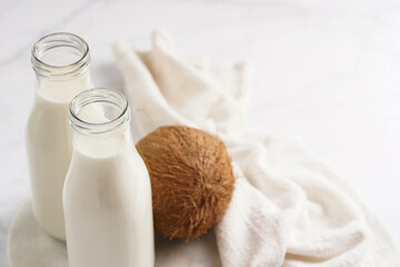 Two bottles with non-dairy milk and coconut on round marble board